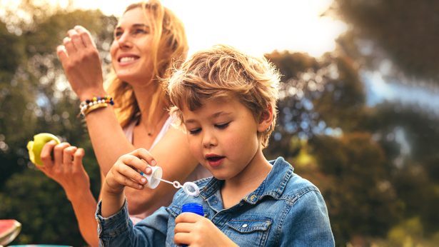 Small kid playing with bubbles at the park with his mother
