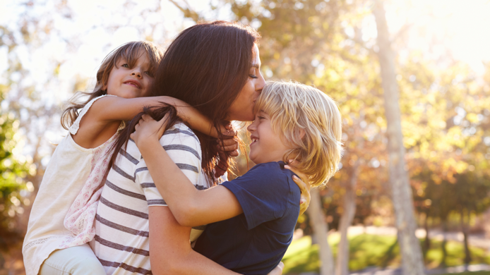 Mother carrying son and daughter as they play in park