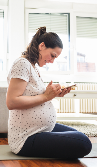 Pregnant woman sitting on the floor in living room, looking at her mobile phone.
