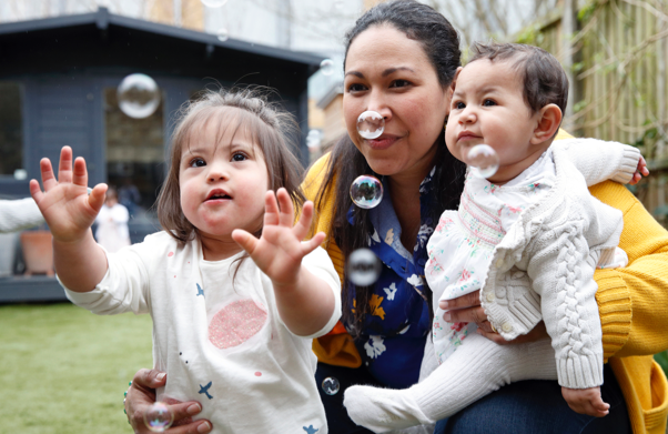 Mother watching bubbles in garden with two daughters