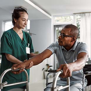 A home health provider assists a member transitioning from his wheel chair to using a walker.