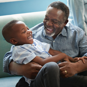 Happy grandfather laughing with grandson on sofa