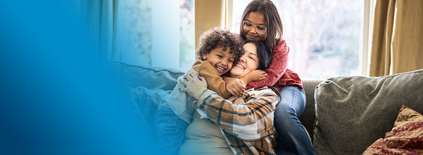  A mother sits on the couch hugging her two children