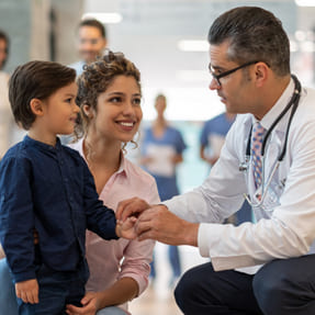 Doctor checking the pulse of a young boy standing with his mother.