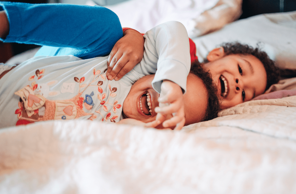 A brother and sister wearing pajamas excitedly laughing and hugging on a bed