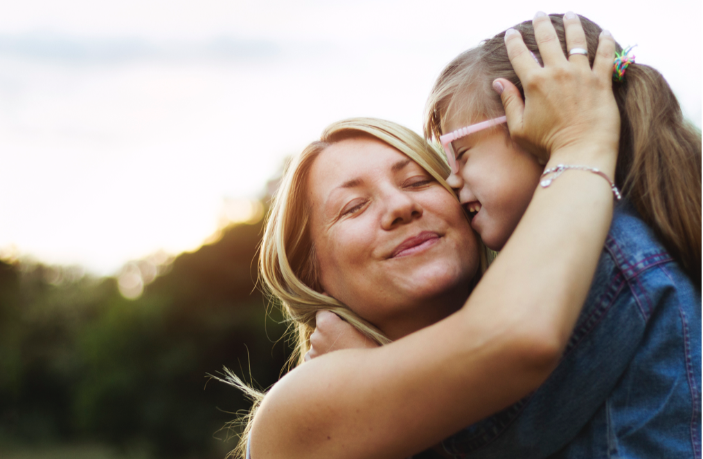 Mother and daughter embracing outdoors with sunset behind them
