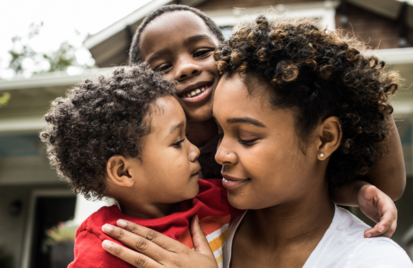 Mother playing with young sons in front of house