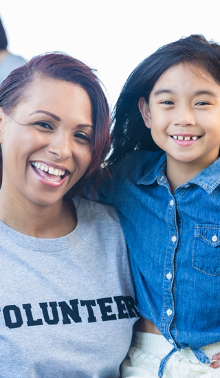 Happy volunteer poses with an elementary age female at a community event
