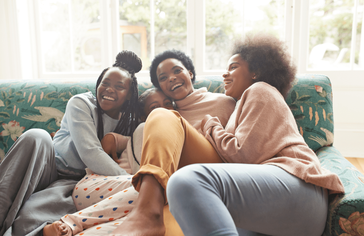 Happy young woman embracing and laughing while sitting on sofa at home