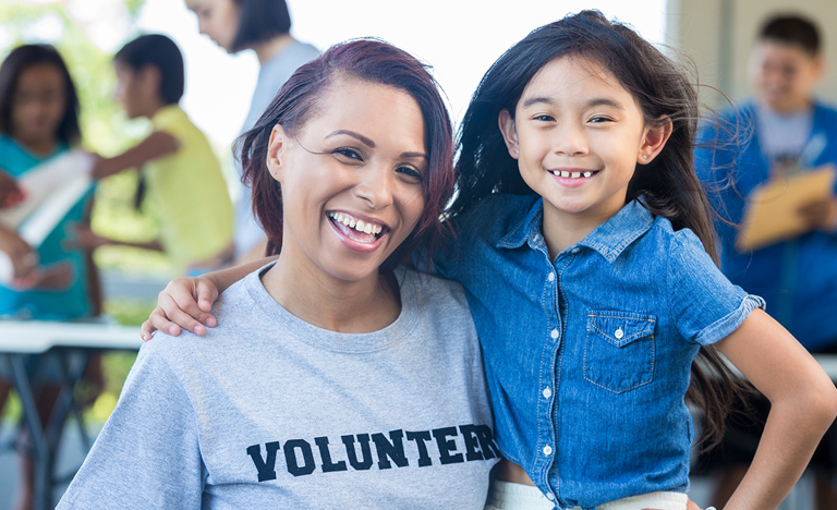 Happy volunteer poses with an elementary age female at a community event
