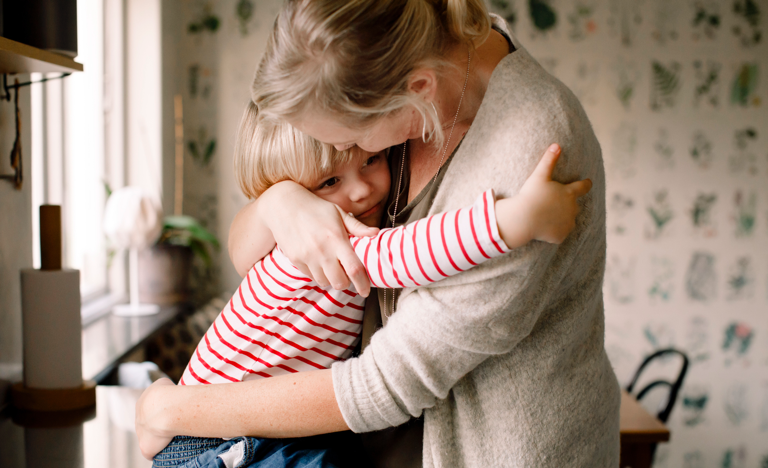 Loving daughter embracing mother while sitting on kitchen counter at home