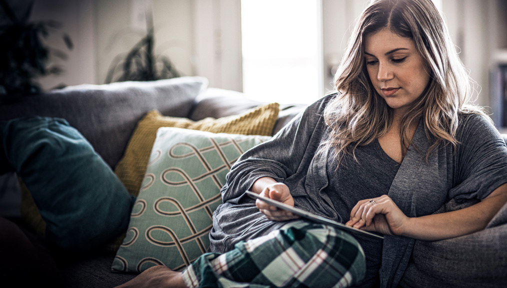 A woman relaxing on her couch while she looks at a iPad.