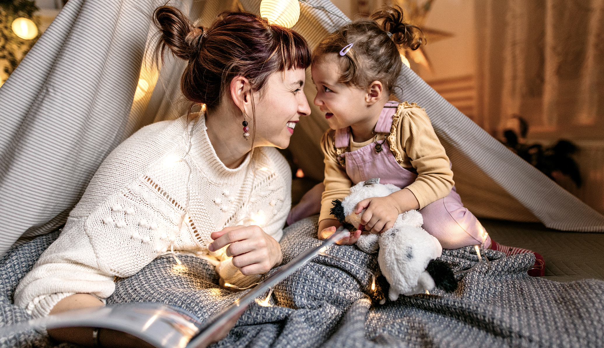 Mother and young daughter smiling and reading together in a makeshift fort