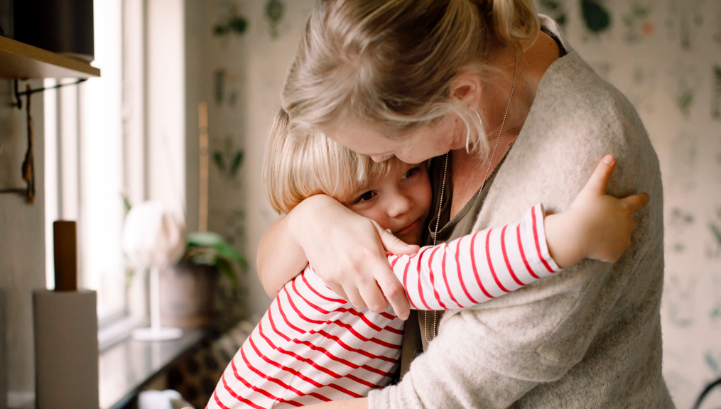 Loving daughter embracing mother while sitting on kitchen counter at home