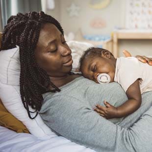 Mother relaxing in bed while her infant sleeps on her chest.